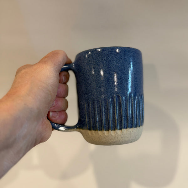 Hand holding a blue ceramic mug against a plain background